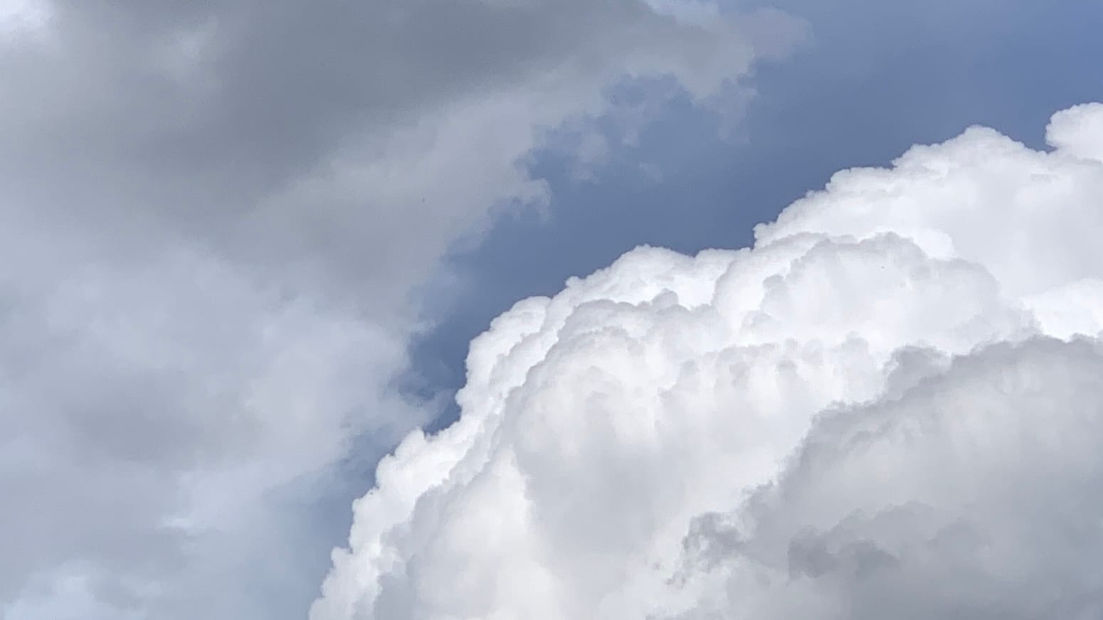 Super puffy and 3-D-looking white clouds lower right with lots of little shadows creating volume appearrance and a bit of dull gray-blue sky behind, and some blurry gray clouds at left