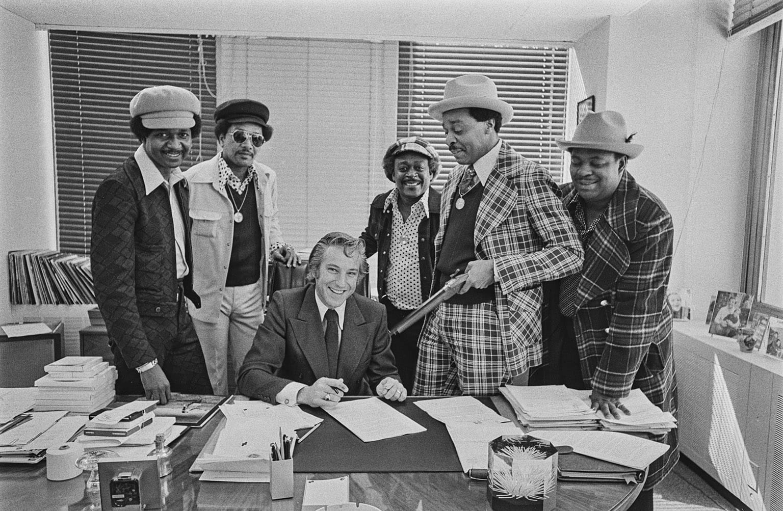 The Dells are dressed well, all wearing stylish hats. Looks like they're there to do some business, maybe sign a contract? Everybody's smiling and the shotgun trained on the guy at the desk seems to be a gag.