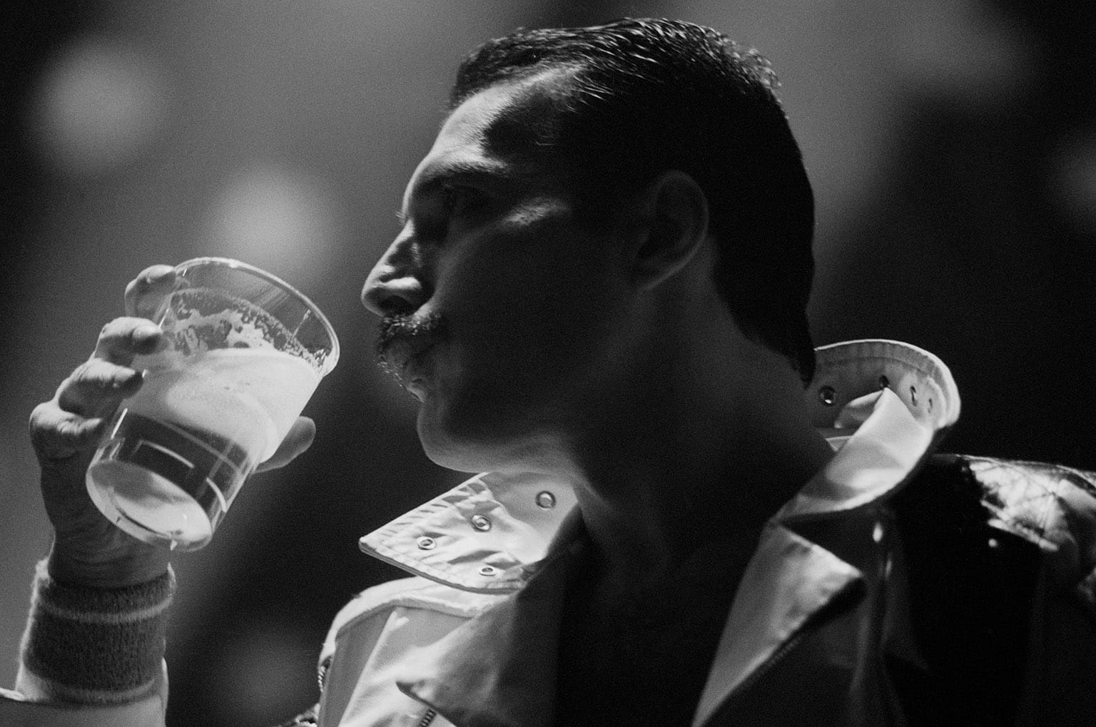 Nice shadowy black & white of Freddie quaffing a plastic cuppa beer as he rocks a white jacket with the collar flipped up.