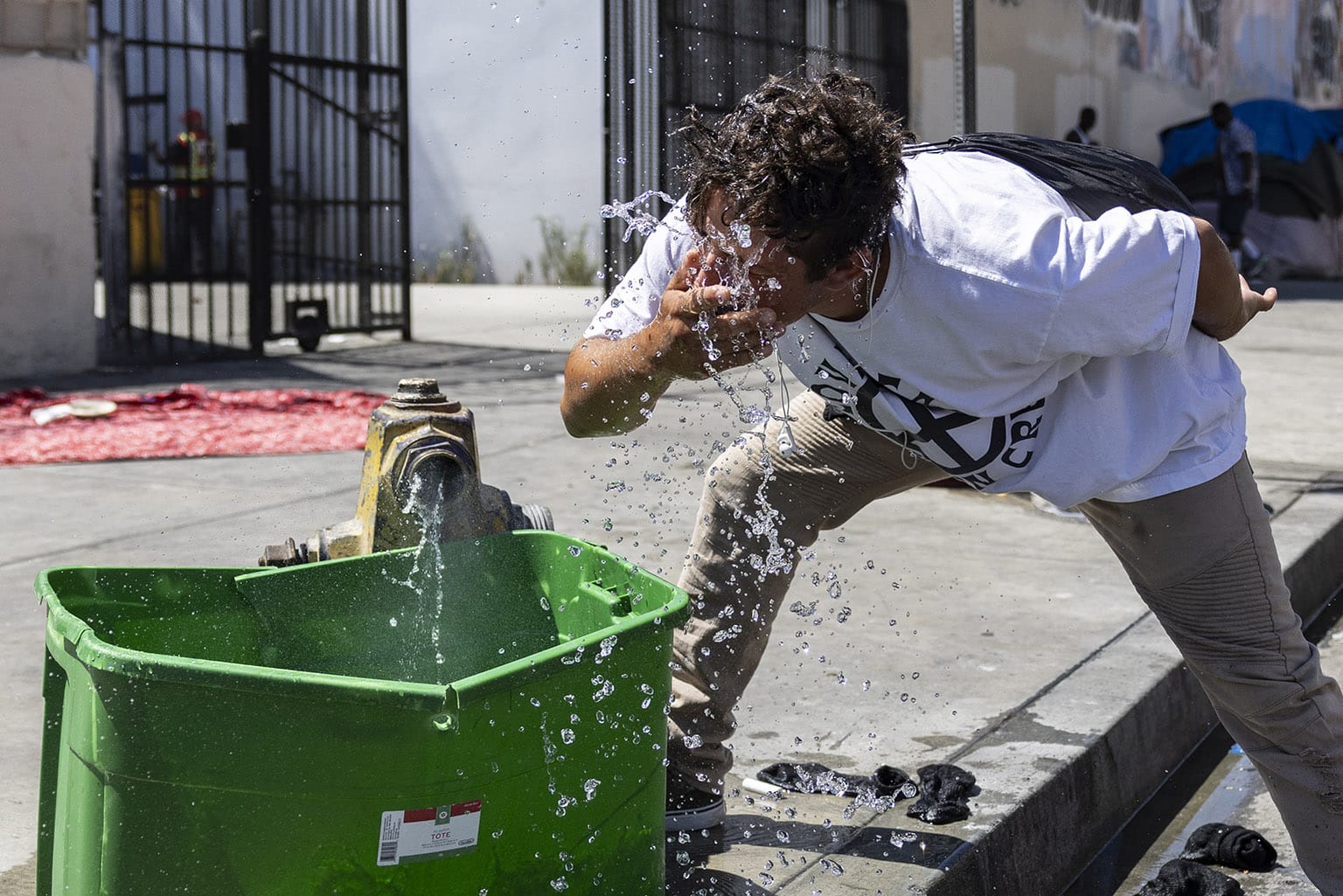 Man splashing his face with hydrant water flowing into a cracked plastic tub