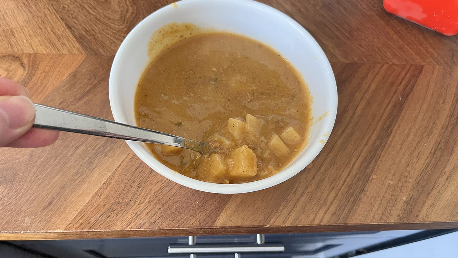 Heated up, now in the bowl, spoon lifting up the potatoes part above the soup waterline.