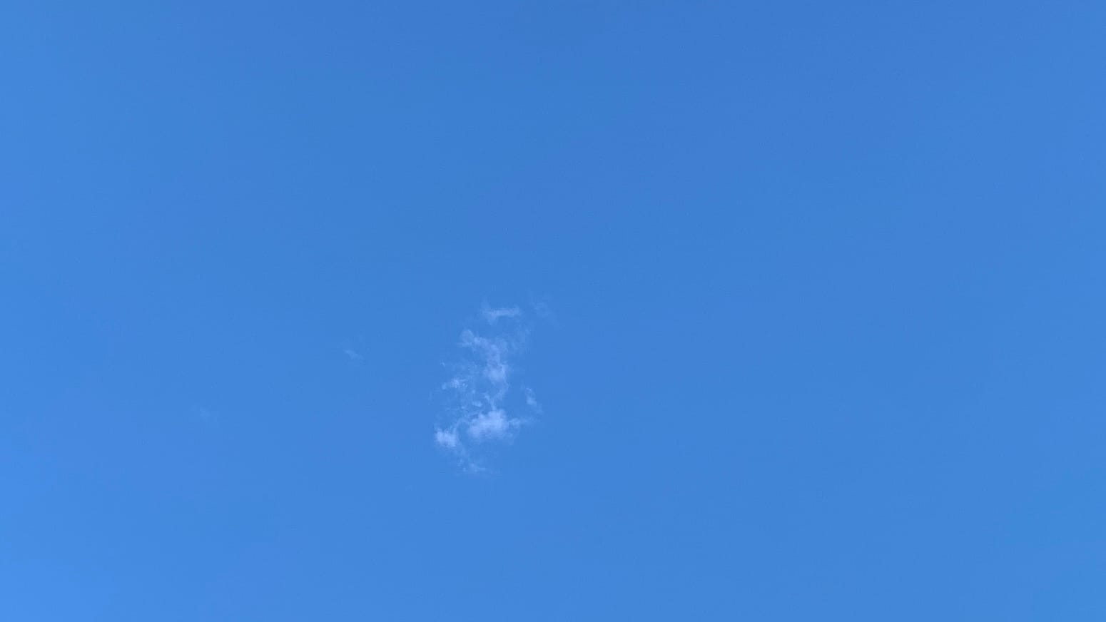 A patch of blue sky with a thin little vertically oriented clump of fractus cloud just to the left of and below the center of the frame. 