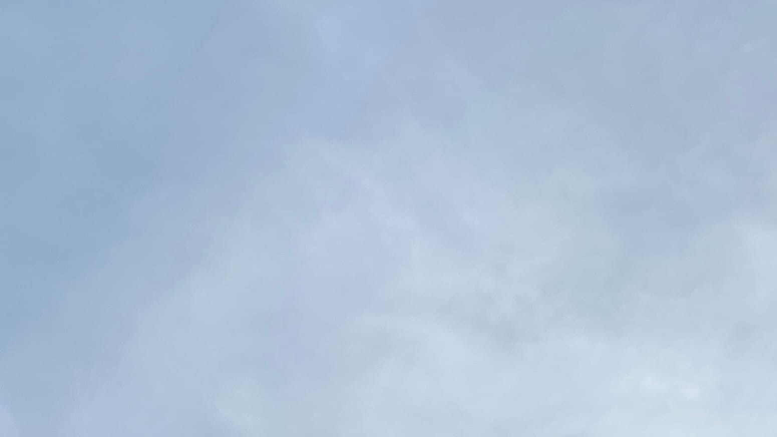 A sky with blue partly showing through a blurry-looking and translucent layer of whitish cloud. The blue is clearest in the upper left corner and the cloud cover is thickest in the lower right. 