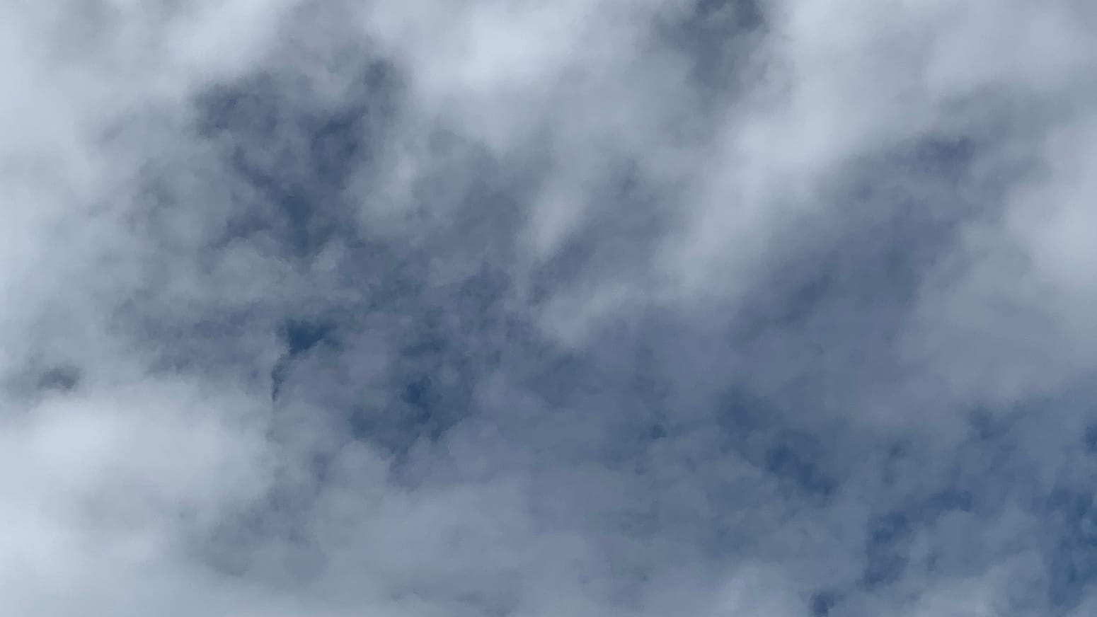 A sky of loose but bright white cloud coming just unclumped enough across the center of the frame to allow deep blue to show through or even to peep through a few small completely clear gaps.  