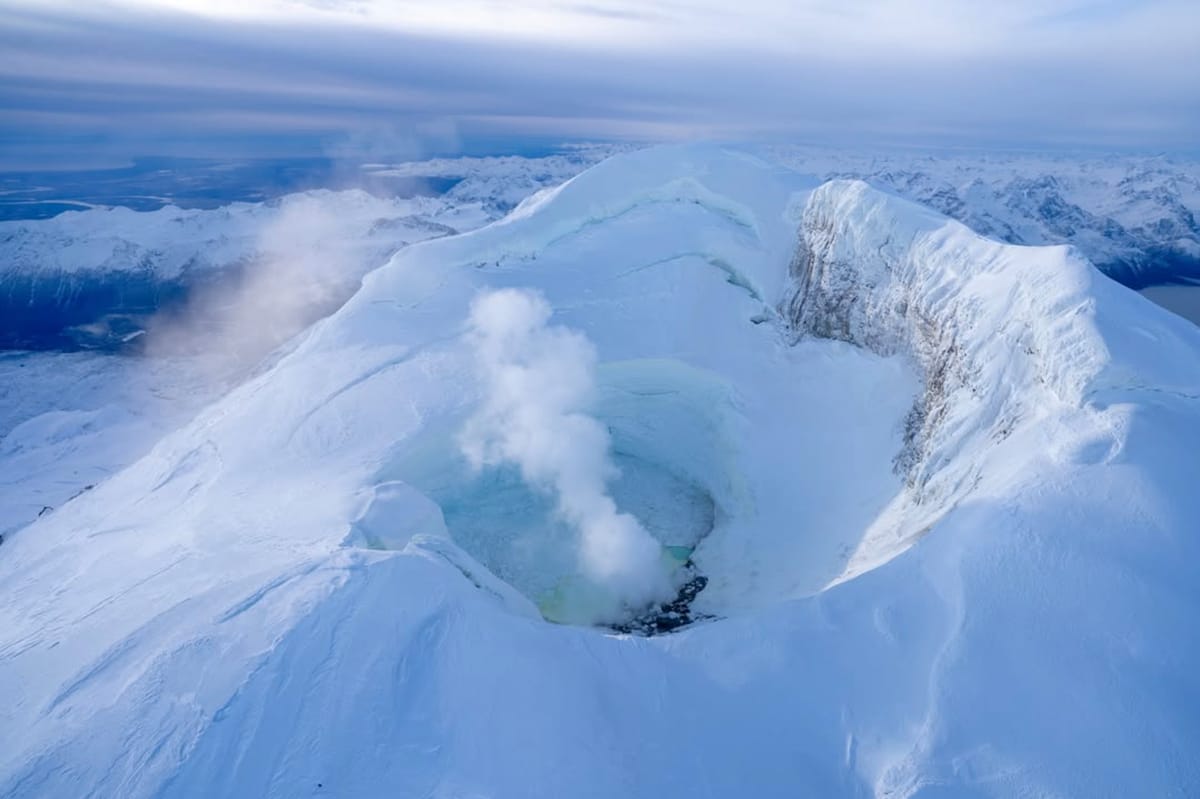 A deeply snow-and-ice-clad summit in the foreground, with a valley backed by many more snowy mountains.