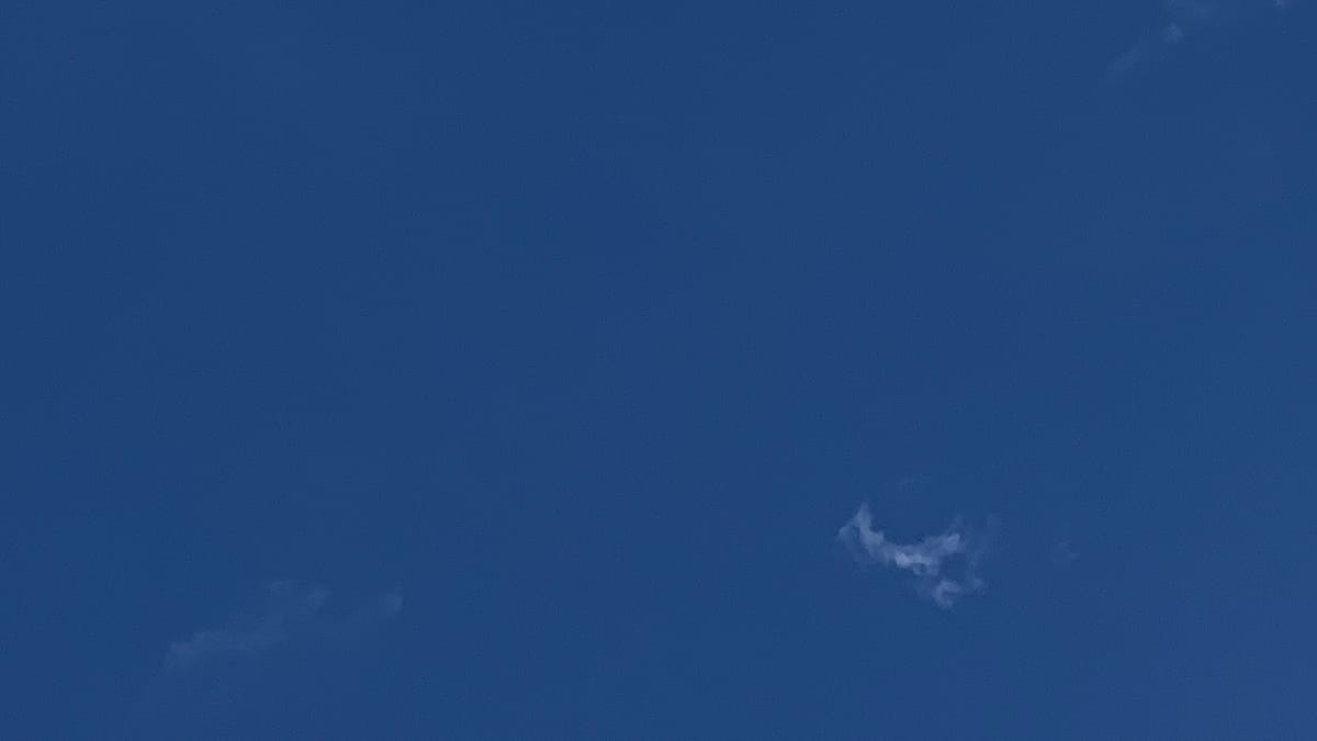 A blue sky with two small shreds of cloud floating in it, one almost invisible