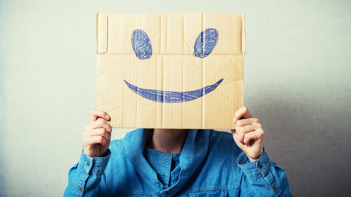 A person holding up a piece of cardboard with a smiley face drawn on it.