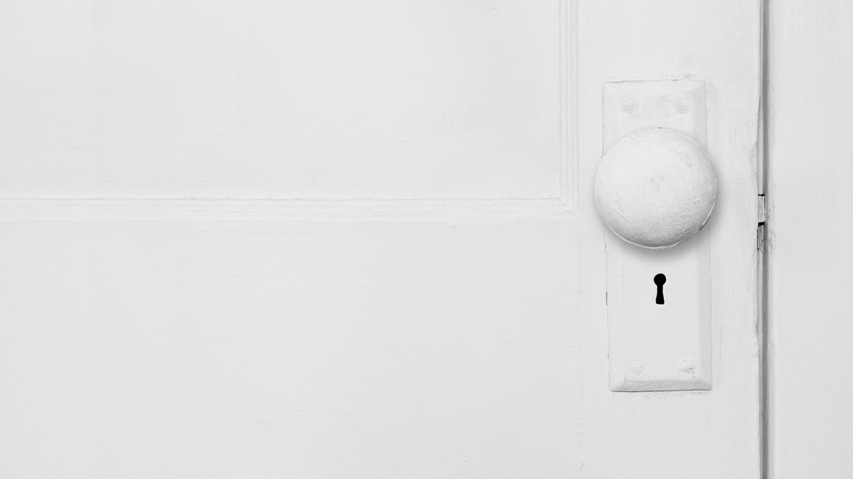 Close-up front view of a white painted door with an old round metal door knob that has been painted white. 