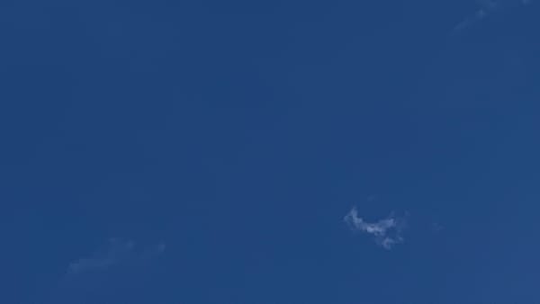 A blue sky with two small shreds of cloud floating in it, one almost invisible